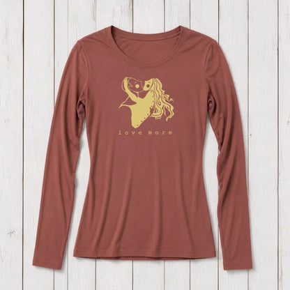 Long sleeve women's graphic t-shirt in rust color with a romantic heart and girl illustration, featuring the words love more, on a white wooden background