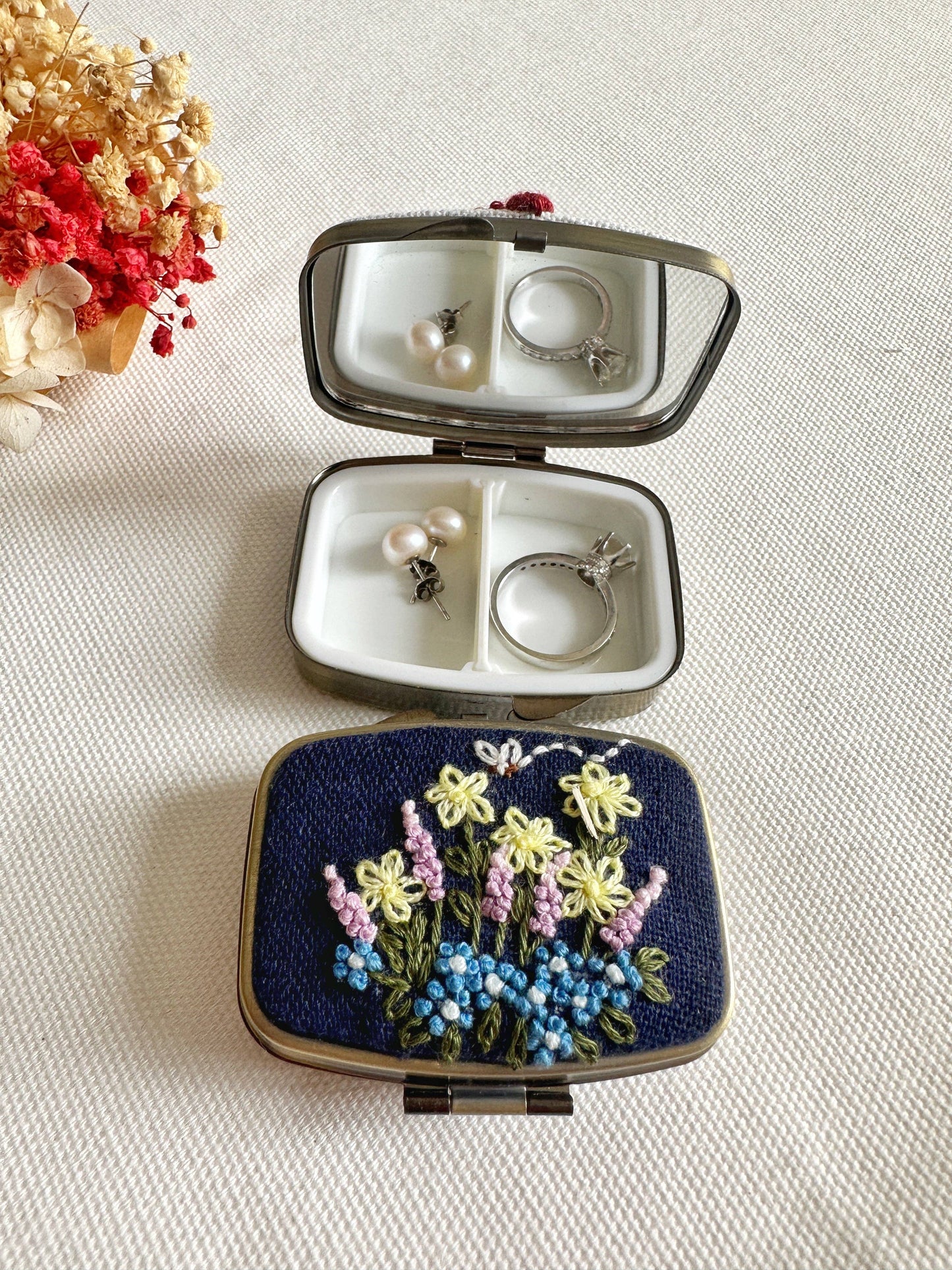 Navy Floral Embroidered Jewelry Box - Elegant Storage with yellow and blue flowers, open to reveal mirror and compartments holding earrings and a ring.