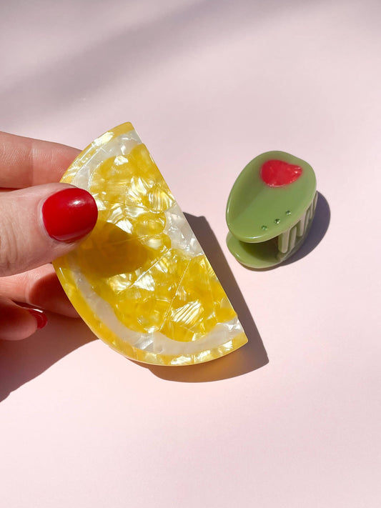 Olive Claw Clip - Cellulose Acetate next to a yellow lemon slice clip, showcasing playful and colorful hair accessories for summer styling.