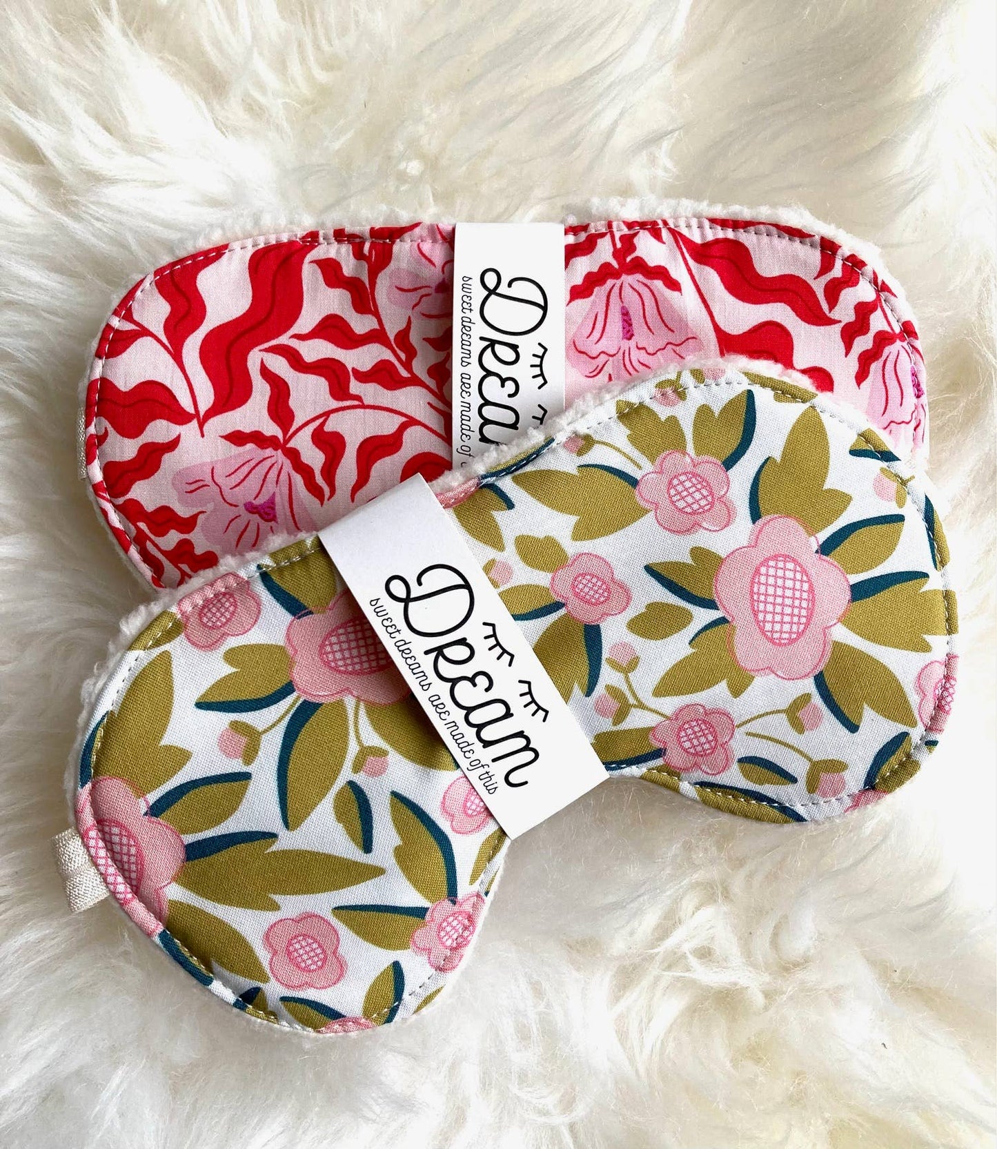 Two Sweet Dreams Cotton Sleep Masks in floral and red swirl prints, ideal for relaxation and restful sleep, shown on plush white fabric.