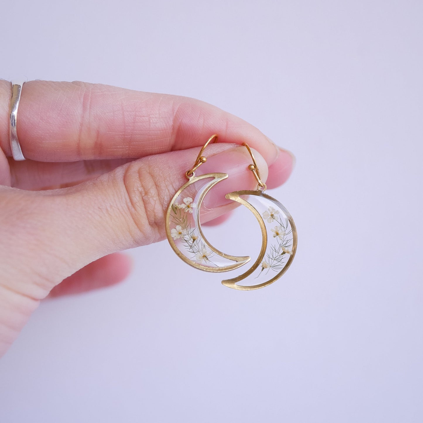 Hand holding brass Garden Flower Earrings with Queen Annes Lace. Lightweight, crescent-shaped flower earrings for botanical jewelry lovers.