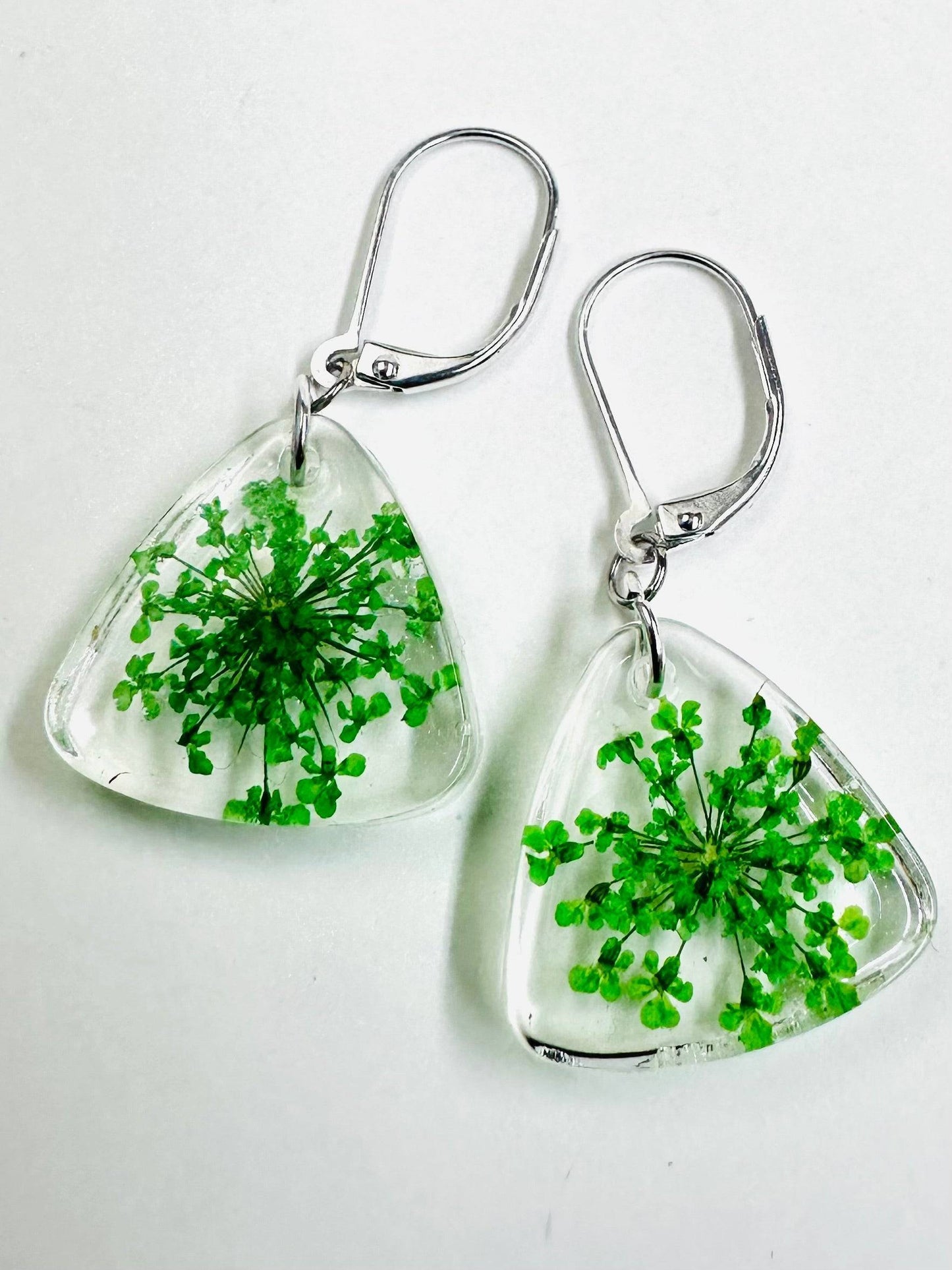 Triangle resin earrings with green flowers and silver hooks. Fresh and vibrant pressed flower earrings with a botanical design.