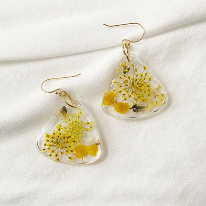 Triangle resin earrings with yellow flowers on white fabric. Real botanical jewelry from the Pressed Flower Earrings collection.