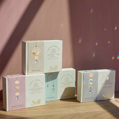 Assorted boxed suncatchers from Scout displayed against a pink wall, showcasing various designs including Blooming Flower Aqua Terra.