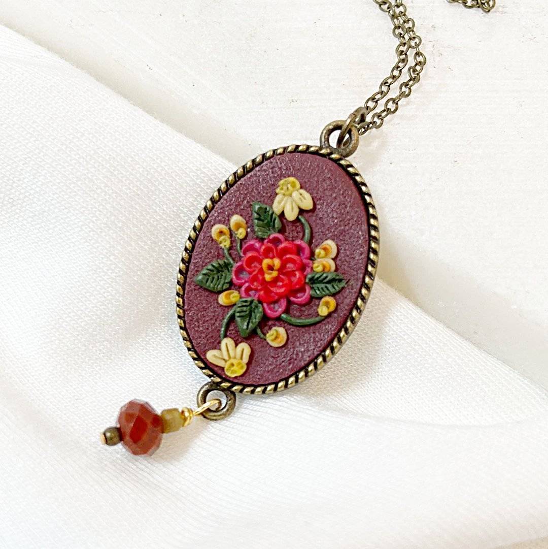 Close-up of Uni-T Polymer Clay Floral Necklace showcasing intricate red and yellow floral design on maroon pendant with faceted red gemstone.