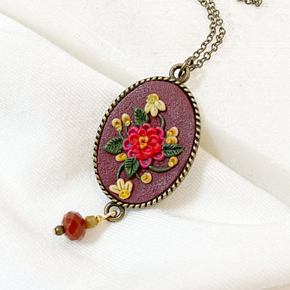 Close-up of Uni-T Polymer Clay Floral Necklace showcasing intricate red and yellow floral design on maroon pendant with faceted red gemstone.