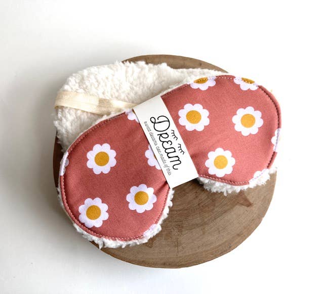 Cotton sleep mask in terra cotta with white daisy print, displayed on a wooden tray with soft Sherpa lining visible. Ideal for restful sleep.