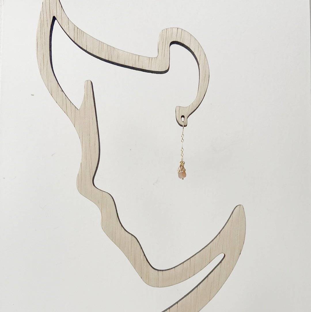 Single drop earring with peach moonstone on a wooden silhouette display, showcasing the Dainty Gemstone Gold Earrings Necklace Set.