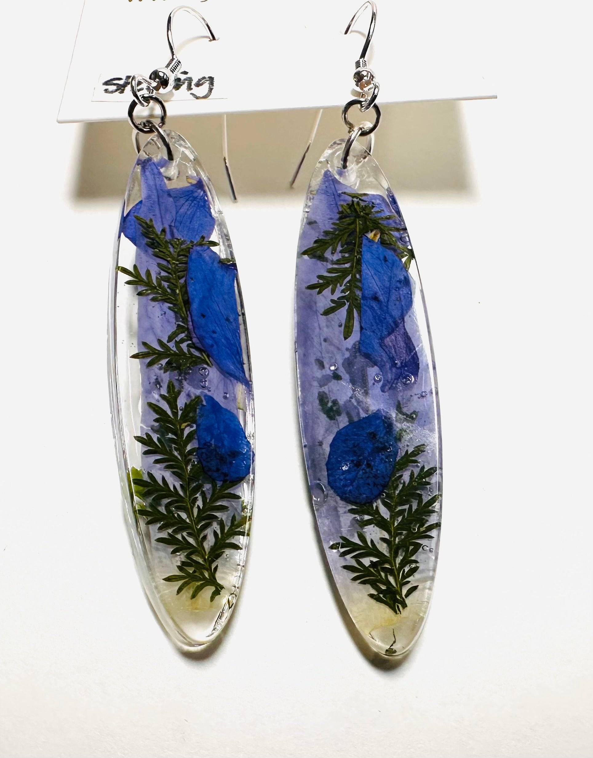 Long oval resin earrings with blue flowers and greenery and silver hooks. Real flower earrings with a cool-toned natural style.