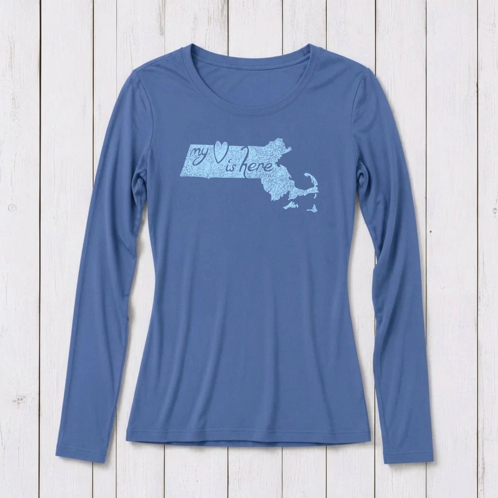 Blue long sleeve T-shirt with a graphic of Massachusetts map and the phrase 'my heart is here' in script, made of organic cotton and bamboo blend, on white wooden background