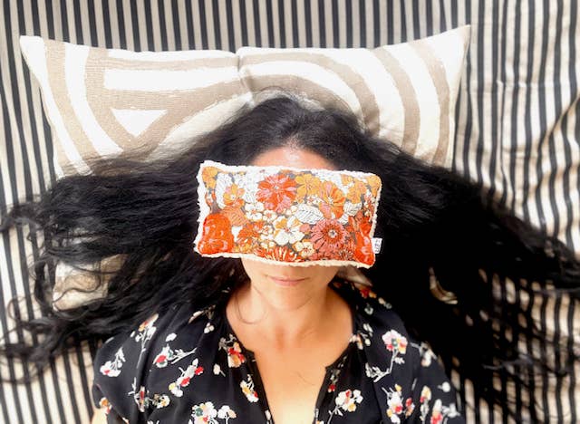Woman using Deep Rest weighted eye pillow in floral print while lying down, demonstrating its use for meditation and deep relaxation.
