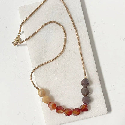Uni-T Beaded Carnelian Necklace with ombré carnelian gemstones and gold seed beads, laid flat to show full design and brass button clasp.