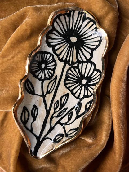 5" handmade floral shaped 22K ceramic catchall jewelry dish with three black outlined flowers and leaves on a velvet fabric background.