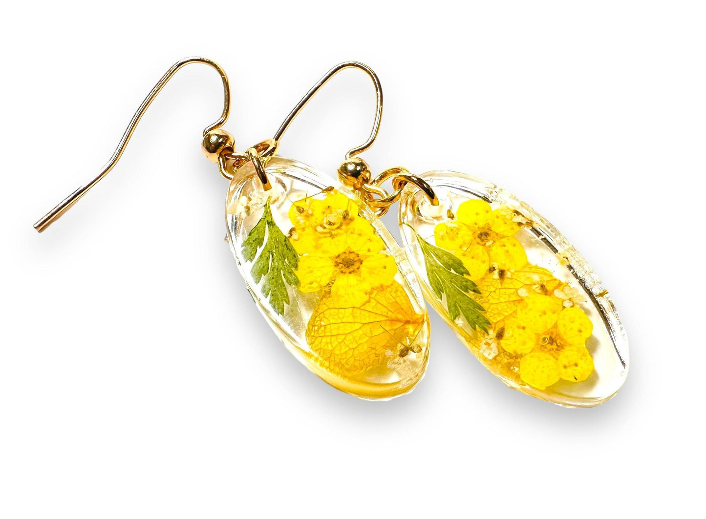 Oval resin earrings with bright yellow flowers and green leaves, featuring gold hooks. Vibrant pressed flower earrings for a sunny look.