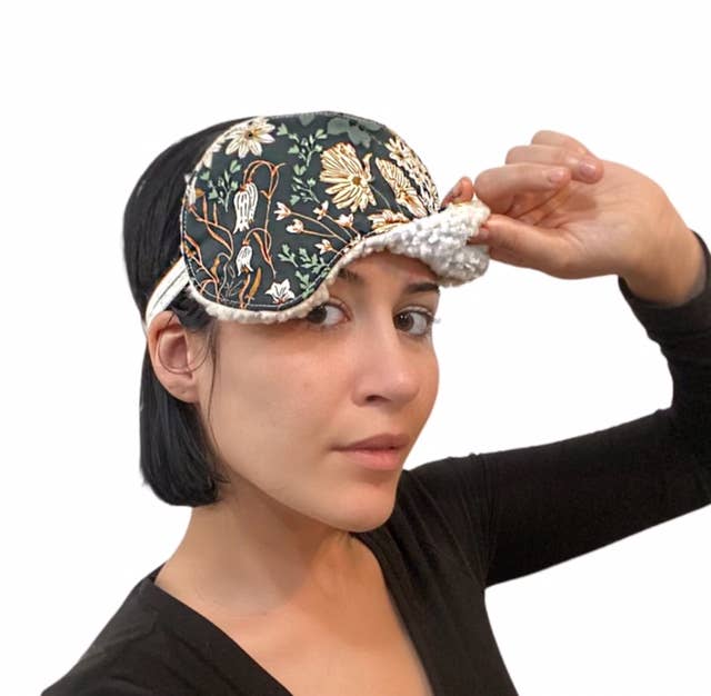 Woman wearing floral version of Le Chat Cotton Sleep Mask, showing soft Sherpa lining and adjustable fit for relaxation and sleep comfort.