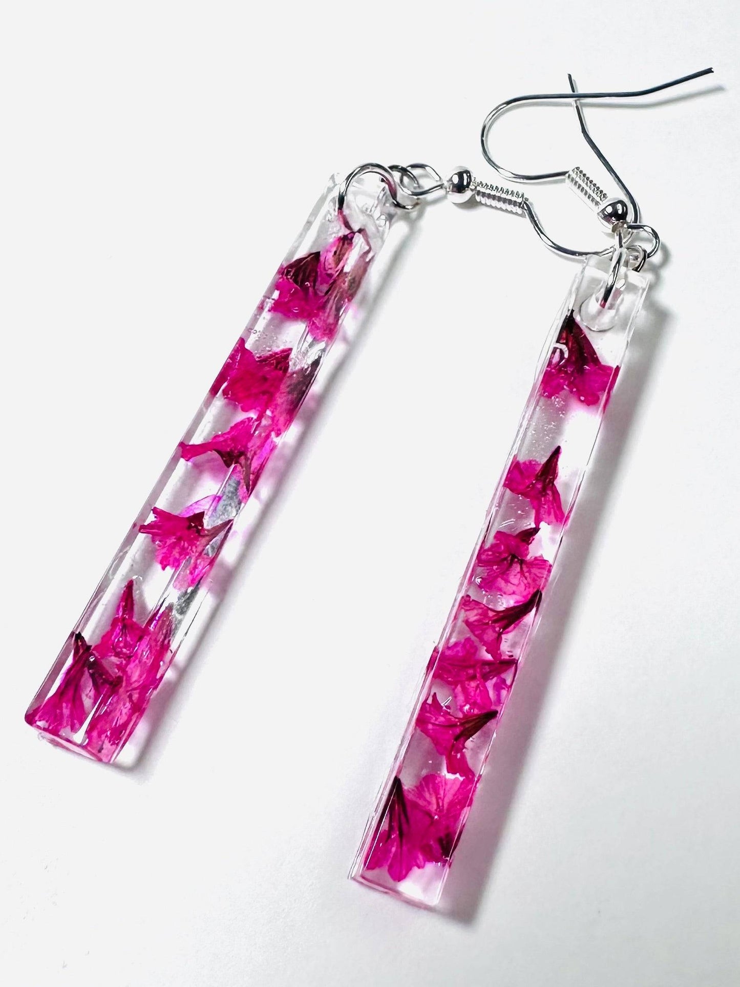 Long rectangular resin earrings with pink petals and silver hooks. Modern pressed flower earrings with a bold pink floral design.