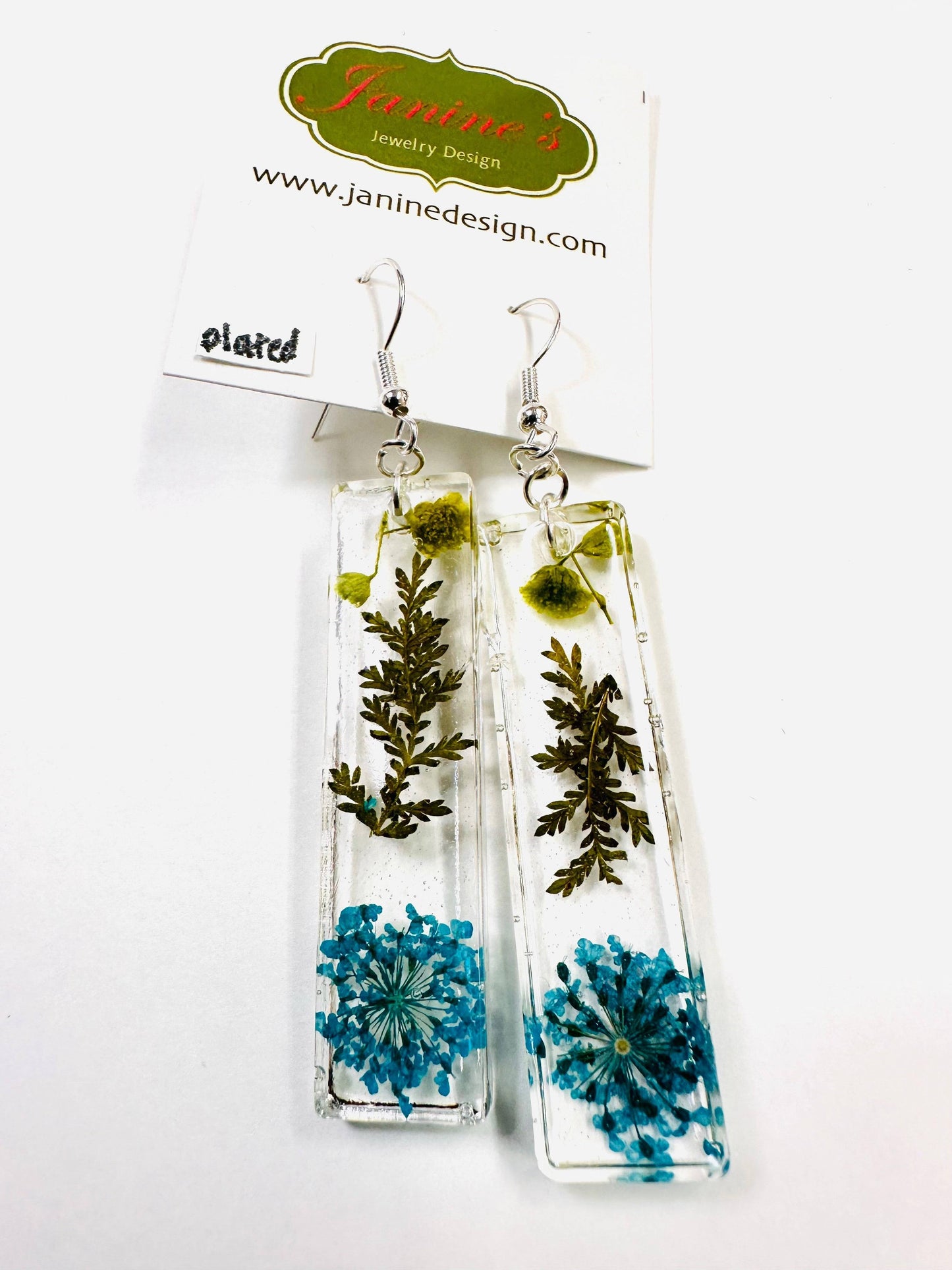 Rectangular resin earrings with blue flowers and greenery and silver hooks. Nature-inspired real flower earrings with a vibrant touch.