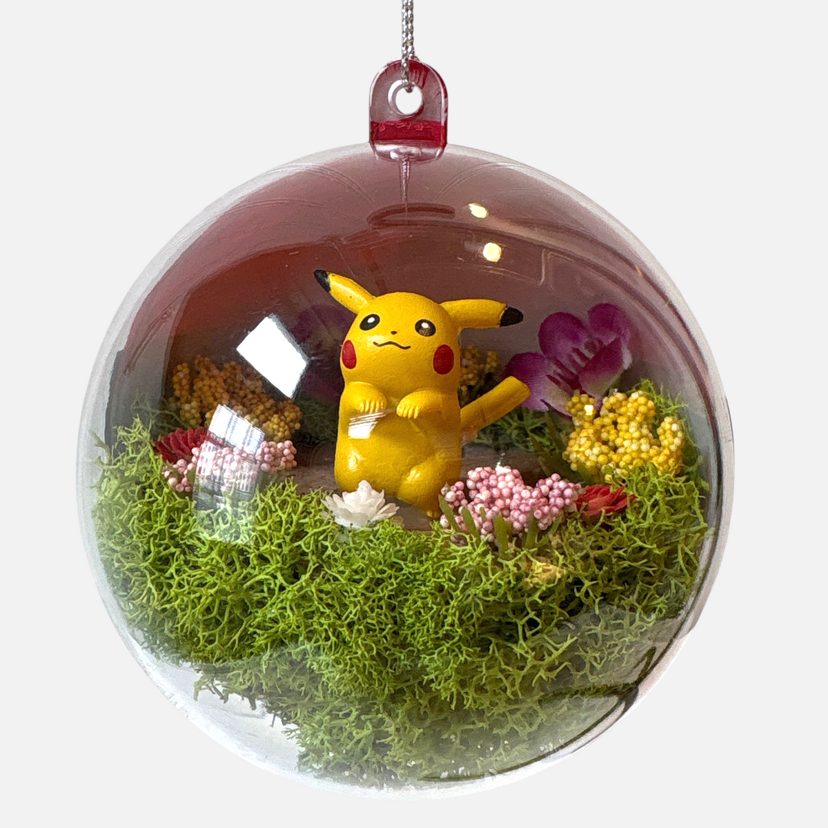 Uni-T Pokeball terrarium ornament featuring a yellow Pikachu figure surrounded by green moss and small floral accents