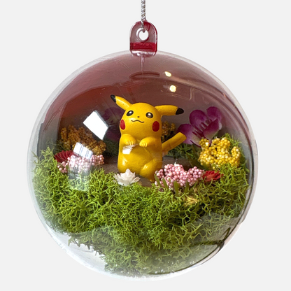 Uni-T Pokeball terrarium ornament featuring a yellow Pikachu figure surrounded by green moss and small floral accents