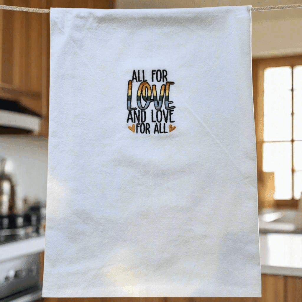 Soft flour sack kitchen towel hanging in a cozy kitchen, featuring rainbow embroidered 'All for Love and Love for All' message at the center.