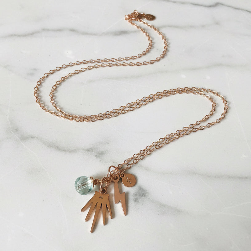 Close-up of gold charm necklace with pearl and lightning bolt charms