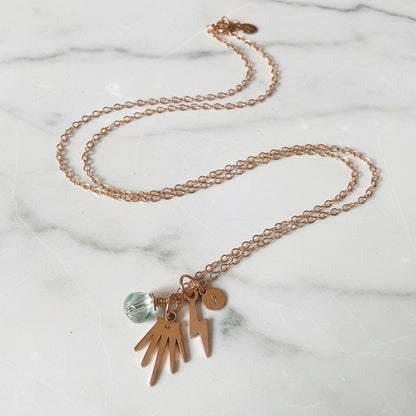 Close-up of gold charm necklace with pearl and lightning bolt charms