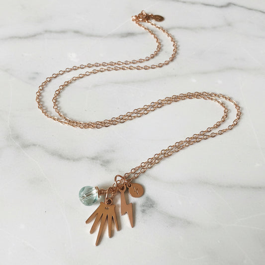 Close-up of gold charm necklace with pearl and lightning bolt charms
