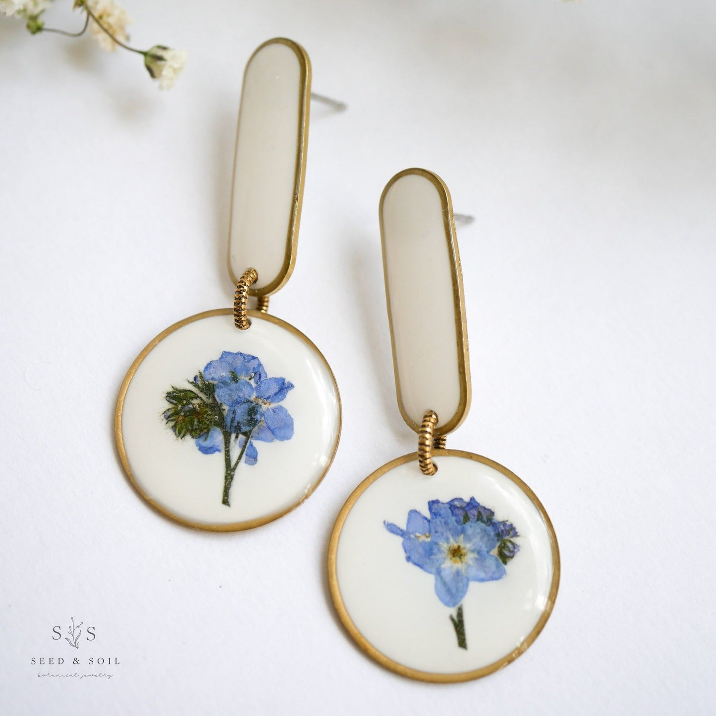 White background Modern Artist Earrings showcasing real blue flowers with stainless steel posts, ideal for artistic expression.