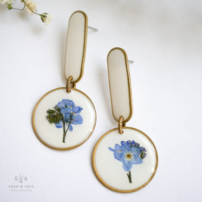 White background Modern Artist Earrings showcasing real blue flowers with stainless steel posts, ideal for artistic expression.