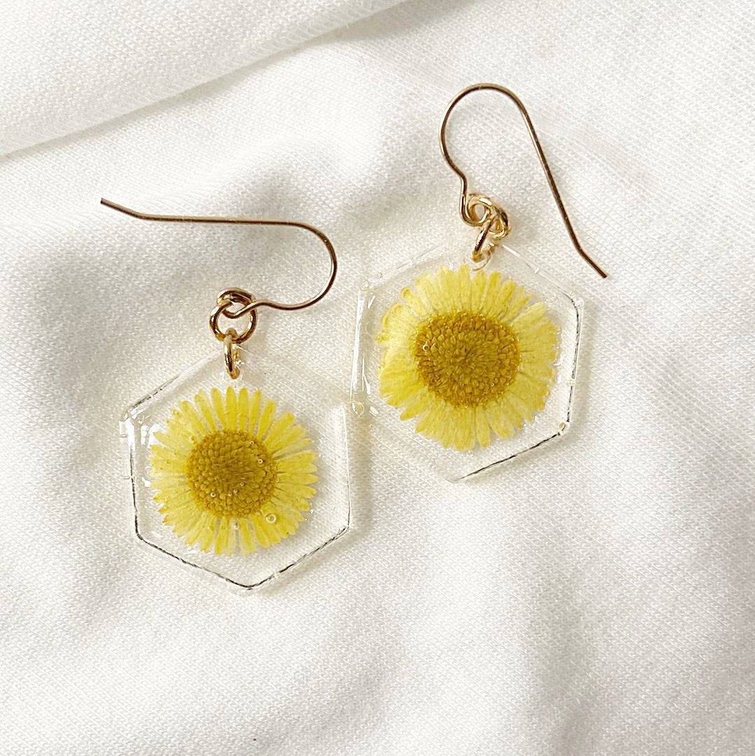 Hexagon resin earrings with yellow daisy flowers on white fabric. Real flower jewelry from the Pressed Flower Earrings collection.