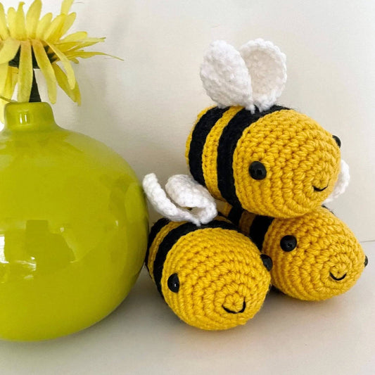 Belinda Bee Stress Ball - Relieve Stress | Compact & Handmade. Three handmade yellow and black crochet bee stress balls stacked beside a green vase with a yellow flower.