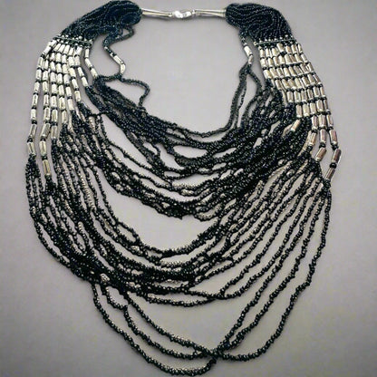 Black beaded statement necklace with layered strands and silver metal accents, perfect for bold fashion looks. Measures 20 to 32 inches in length.