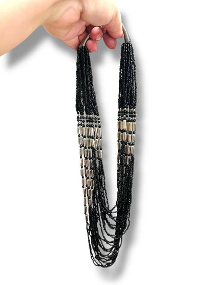 Hand holding a long black beaded necklace with silver tube beads, showcasing its elegant drape and statement style for jewelry collections.