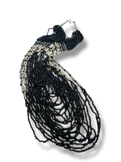 Black beaded necklace with cascading strands and silver accents laid flat, highlighting its intricate design and adjustable 20–32 inch length.
