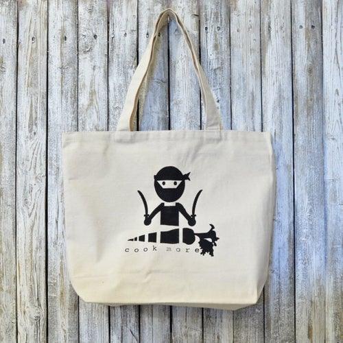 Culinary tote bag organic with COOK MORE artist design featuring a ninja chef graphic, made from 100% cotton. Ideal for eco-conscious cooking lovers.