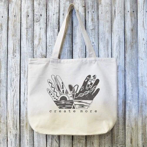 Create More with Organic Canvas Artist Tote Bag featuring illustrated hands and creative elements. Eco-friendly and ideal for artists and creators.