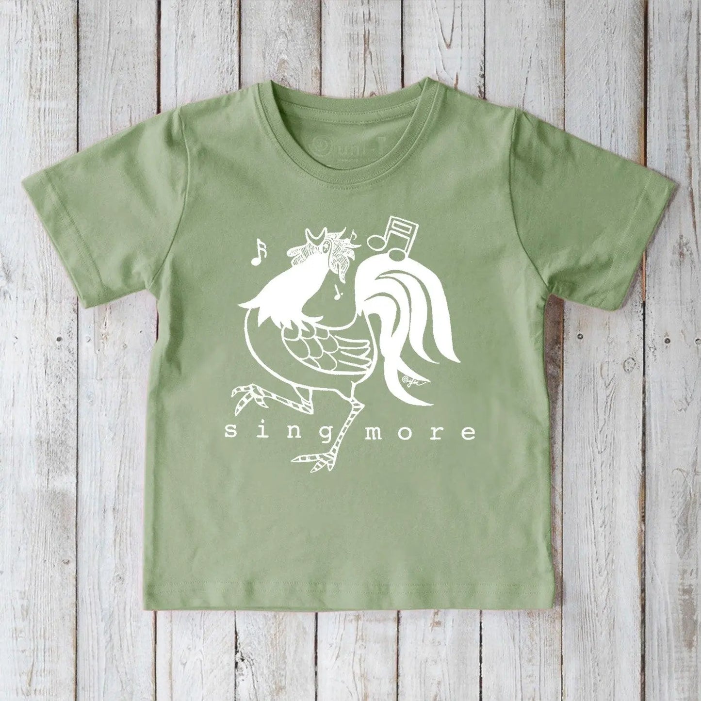 Green organic cotton kids' t-shirt featuring a fun rooster and 'Sing More' design, sustainable and playful farm-themed apparel.
