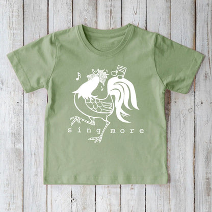 Green organic cotton kids' t-shirt featuring a fun rooster and 'Sing More' design, sustainable and playful farm-themed apparel.