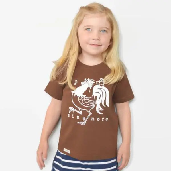 Girl wearing brown 'Sing More' rooster t-shirt made from organic cotton, showcasing a fun and sustainable kids' graphic tee.