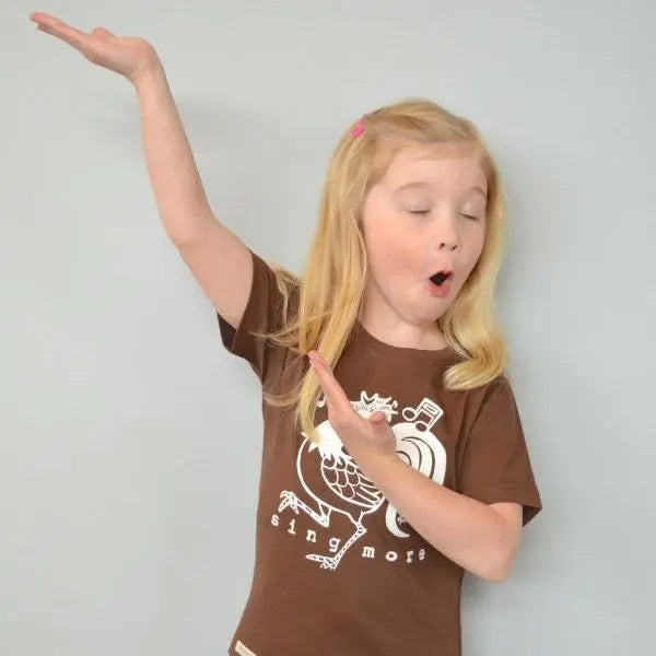 Child playfully posing in brown rooster graphic tee with 'Sing More' text, organic cotton shirt for kids with fun animal design.