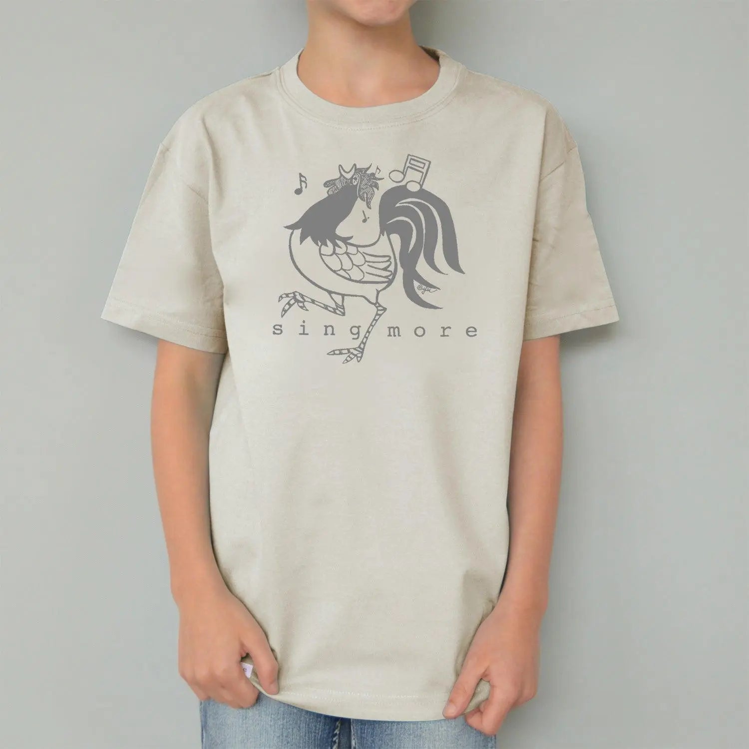 Child in cream rooster t-shirt with 'Sing More' print, organic cotton kids' top with eco-friendly farm animal graphic.