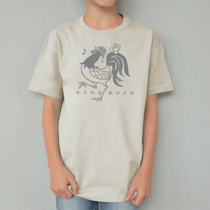 Child in cream rooster t-shirt with 'Sing More' print, organic cotton kids' top with eco-friendly farm animal graphic.