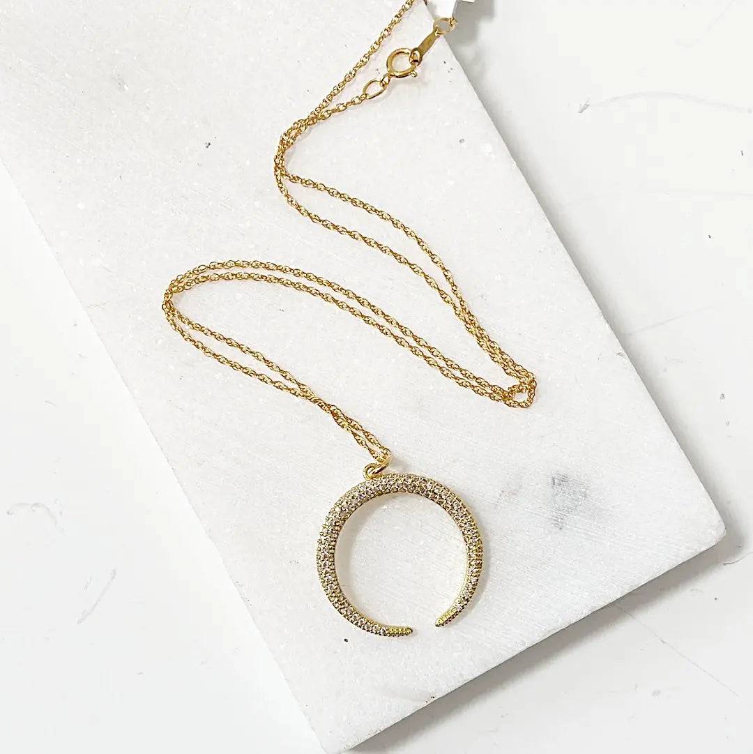 Gold crescent moon necklace with cubic zirconia on an 18” rope chain, displayed on a white marble background. Elegant and ideal for layering.
