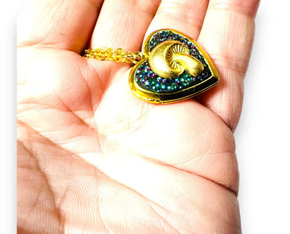 Heart-shaped brass locket with mushroom and rainbow crystal clay held in hand, showing its compact and wearable size.