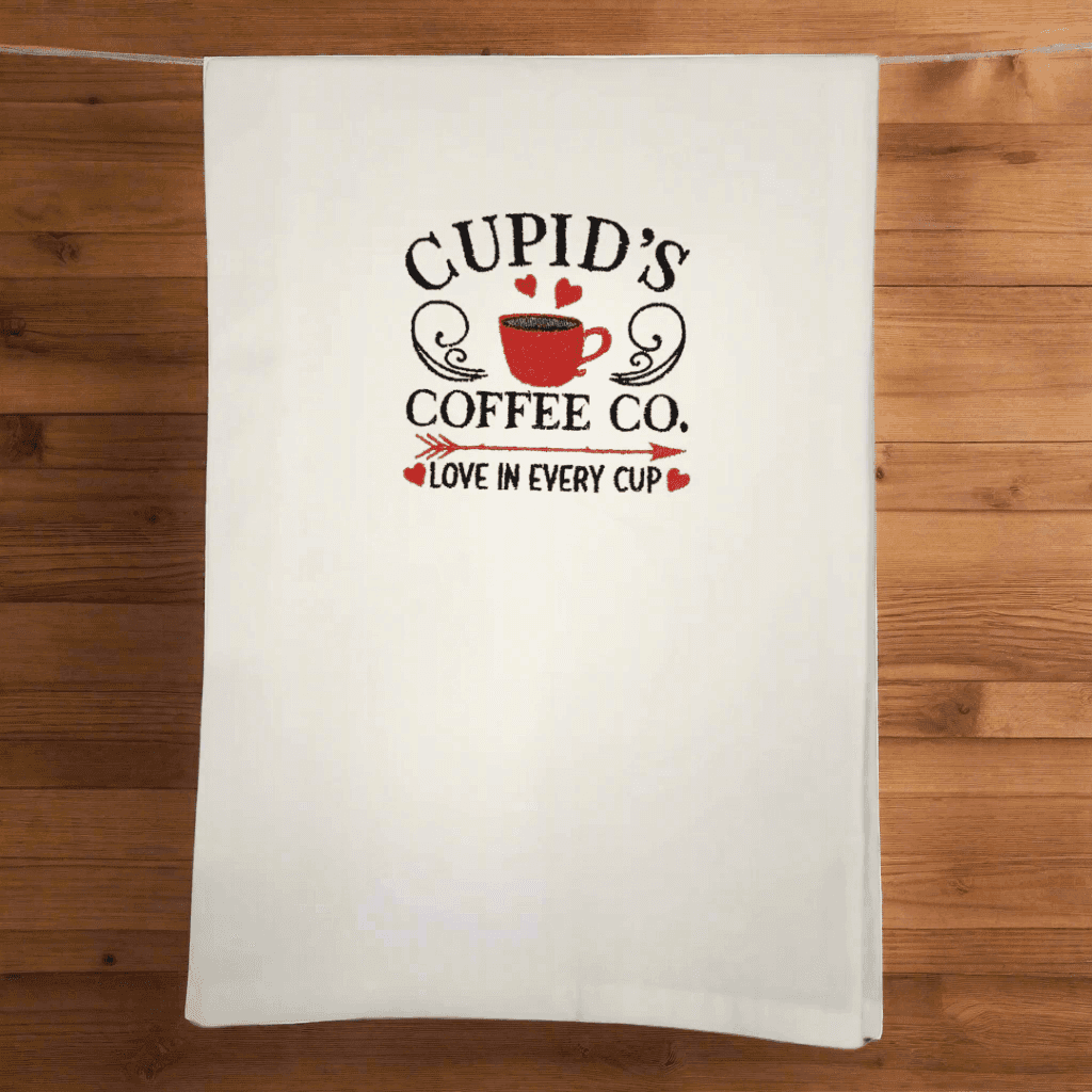 Cupid's Coffee Co. Towel - Embroidered Kitchen Towel hanging on wooden background, perfect for coffee lovers and stylish kitchens.