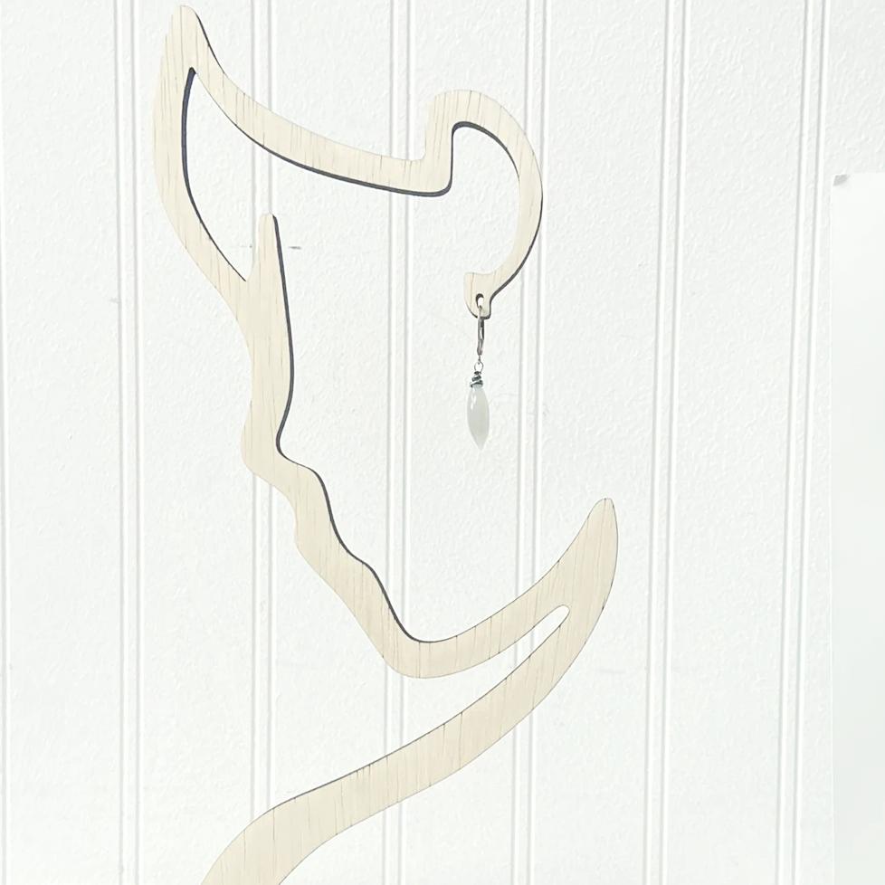 Single Moonstone Dagger Earring displayed on abstract wooden stand. Features sterling silver hook and faceted moonstone bead for modern style.