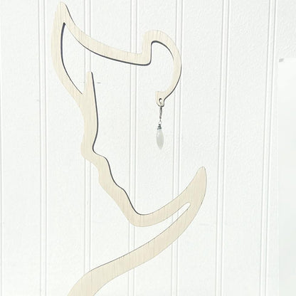 Single Moonstone Dagger Earring displayed on abstract wooden stand. Features sterling silver hook and faceted moonstone bead for modern style.