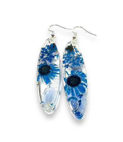 Oval earrings with blue daisy flowers in resin and silver hooks. Real flower earrings with a fresh botanical design.