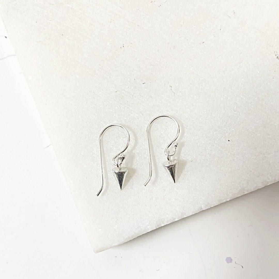 Sterling silver Tiny Spike Earrings-Uni-T featuring pointed spike charms on hooks, laid flat on a white stone background for detail view.
