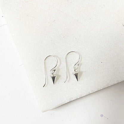 Sterling silver Tiny Spike Earrings-Uni-T featuring pointed spike charms on hooks, laid flat on a white stone background for detail view.